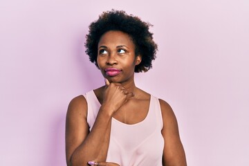 Young african american woman wearing casual sleeveless t shirt with hand on chin thinking about question, pensive expression. smiling with thoughtful face. doubt concept.