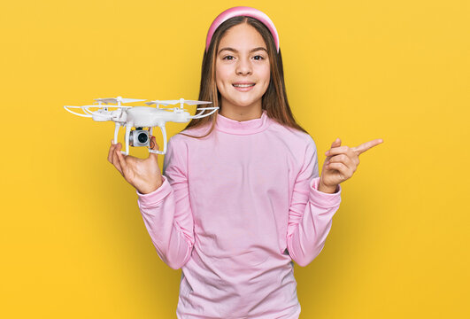 Beautiful brunette little girl using drone smiling happy pointing with hand and finger to the side
