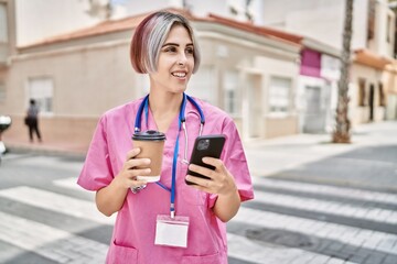 Young caucasian doctor woman drinking coffee and using smartphone at the city.
