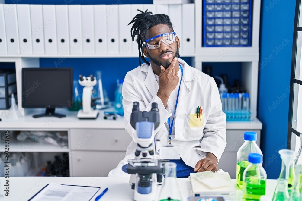 Wall mural african man with dreadlocks working at scientist laboratory thinking concentrated about doubt with f