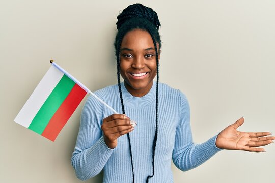 African american woman with braided hair holding bulgaria flag celebrating achievement with happy smile and winner expression with raised hand