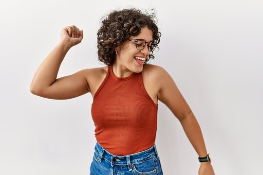 Young hispanic woman wearing glasses standing over isolated background dancing happy and cheerful, smiling moving casual and confident listening to music