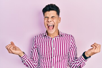 Young hispanic man wearing casual clothes celebrating mad and crazy for success with arms raised and closed eyes screaming excited. winner concept