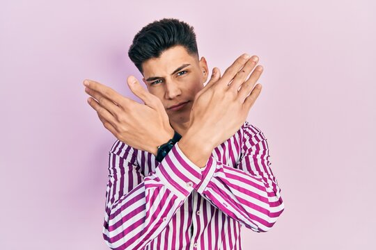 Young hispanic man wearing casual clothes rejection expression crossing arms and palms doing negative sign, angry face