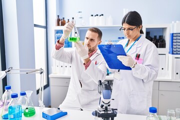 Man and woman wearing scientists uniform measuring liquid at laboratory