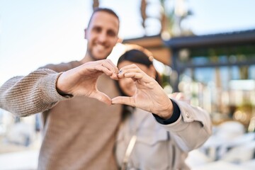 Man and woman smiling confident doing heart symbol with hands at street