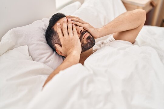 Young hispanic man stressed lying on bed at bedroom