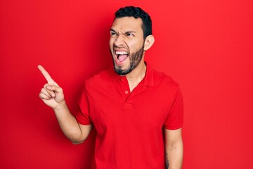 Fototapeta premium Hispanic man with beard pointing with fingers to the side angry and mad screaming frustrated and furious, shouting with anger. rage and aggressive concept.