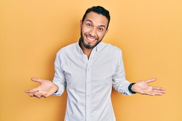 Hispanic man with beard wearing business shirt clueless and confused expression with arms and hands...