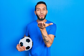 Hispanic man with beard holding soccer ball looking at the camera blowing a kiss with hand on air being lovely and sexy. love expression.