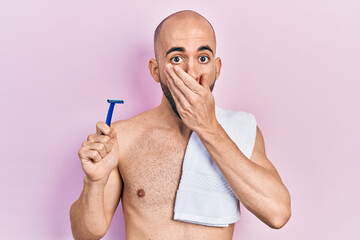 Young bald man shirtless holding razor covering mouth with hand, shocked and afraid for mistake. surprised expression