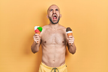 Fototapeta premium Young bald man wearing swimwear holding two ice cream cones angry and mad screaming frustrated and furious, shouting with anger looking up.
