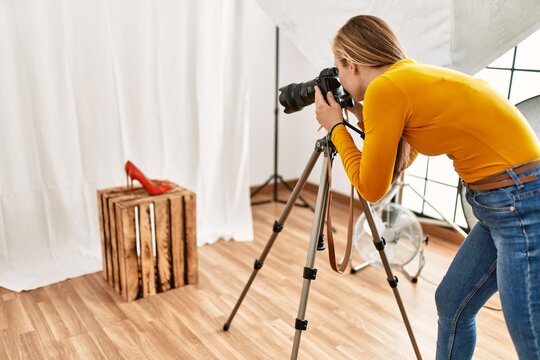 Young caucasian woman photographer making photo to high heel shoe at photography studio