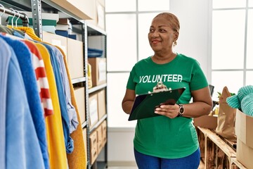 Senior african american woman wearing volunteer uniform writing on clipboard at charity center