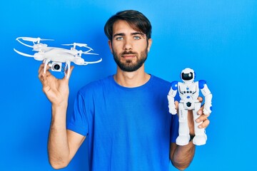 Fototapeta na wymiar Young hispanic man holding drone and robot toy relaxed with serious expression on face. simple and natural looking at the camera.
