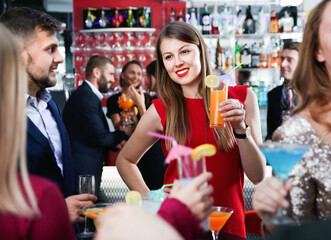 Young happy cheerful positive attractive woman with cocktails having fun with friends at nightclub