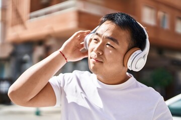 Young chinese man smiling confident listening to music at street