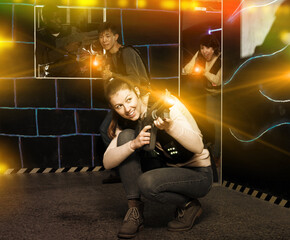 Emotional girl with laser pistol playing laser tag with multinational team on dark labyrinth