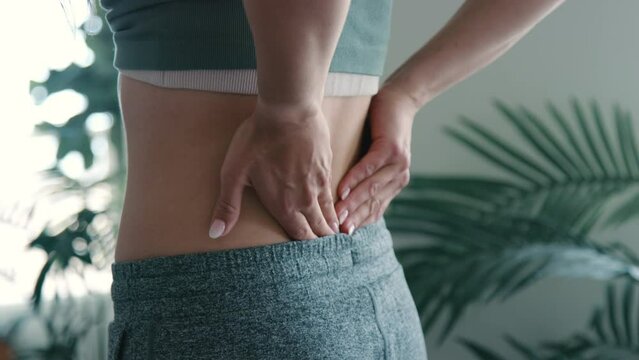Young hispanic woman aggressively massages low back muscles in slow motion