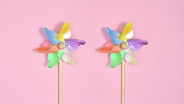 Colorful plastic windmills spins on pastel pink background. Stop motion flat lay