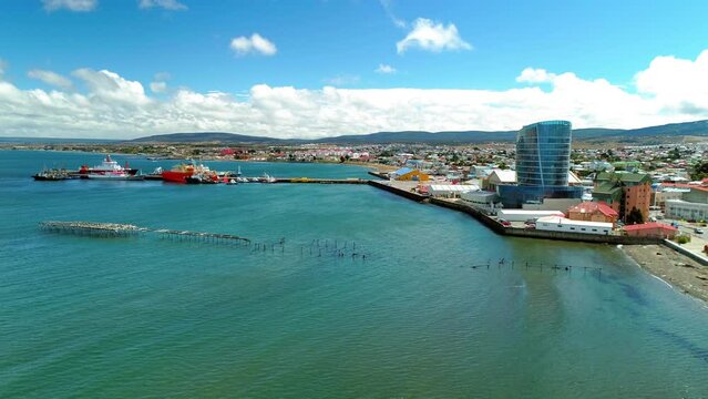 Aerial Modern Building In Town By Hills, Drone Flying Backwards Over Sea On Sunny Day - Punta Arenas, Chile