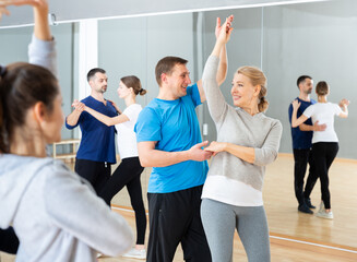 Middle-aged woman and man practicing bachata dance moves in pair during group class