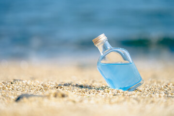  A glass bottle of blue water on the beach on sunny day, Tropical summer vacation background