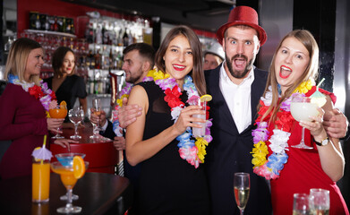 Happy young man with female friends enjoying party in Hawaiian style in bar