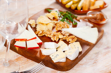 Varieties of cheese sliced and served on wooden board with walnuts and honey.