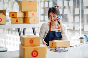 Startup small business entrepreneur or freelance Asian woman using a laptop with box, Young success Asian woman with her hand lift up, online marketing packaging box and delivery, SME concept.