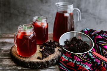 Agua de Jamaica or roselle mocktail drink, summer beverage in mexico with ice and dry hibiscus petals on table background - obrazy, fototapety, plakaty