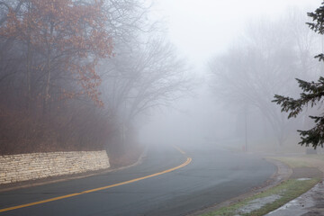 Road with double yellow lines winding through a heavy fog on a winter day