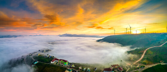 Aerial view top hill at dawn with fog covering small village in valley, beautiful wind power poles...