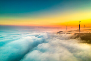 Aerial view top hill at dawn with fog covering small village in valley, beautiful wind power poles...