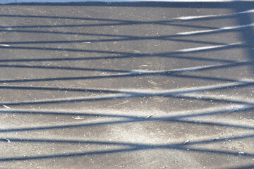 The shadow from the fence on the asphalt road.