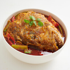Bowl of spicy Asian curry fish head dish decorated with spices and ingredients isolated on white background