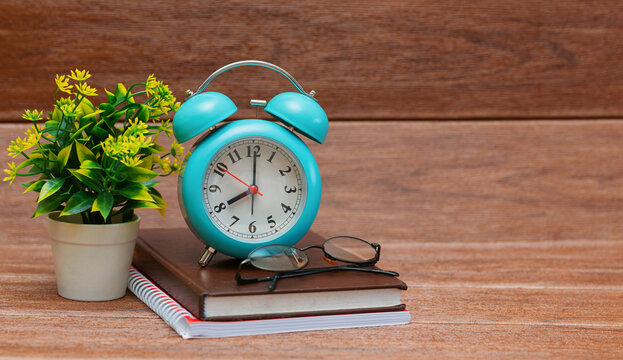 Colorful alarm clock, books, glasses on wooden table on wood grain background. back to school concept