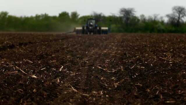 A modern tractor with sows a field. . A farmer on a tractor plows dusty arid soil and sows cereal grains. Agribusiness in the spring. Agricultural work in the fields, agribusiness. Selective focusing
