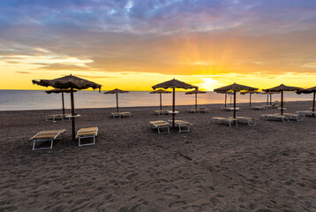  empty beach during beautiful sunrise or sunset with chaise loungues and nice umbrellas with blue sea