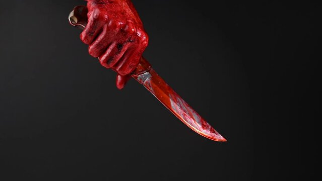 Man holding knife with bloody hand on black background. 