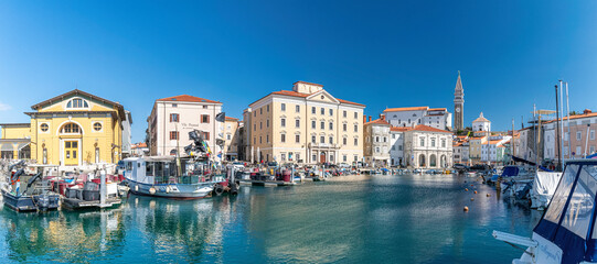 Mediterranean sunny port in slovenia, harbour view city of piran, old mediterranean houses and ships in the bay. Skyline with clocktower in back