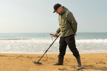A man with a metal detector and a shovel on the seashore. A treasure hunter with a metal detector. A man is looking for a treasure.