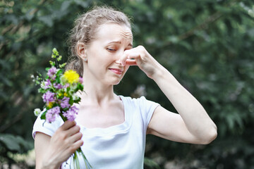 Allergy. Woman squeezed her nose with hand, so as not to sneeze from the pollen of flowers