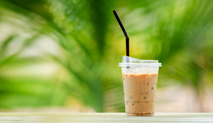 Iced coffee in tall glass, ice cubes. Cool summer drink with straws on warm natural green blur background. copy space - obrazy, fototapety, plakaty