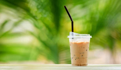 Rolgordijnen Iced coffee in tall glass, ice cubes. Cool summer drink with straws on warm natural green blur background. copy space © FOTO SALE