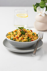 Table setting with tabule salad bowl made with bulgur and vegetables and dressing with olive oil and lemon juice on the table with glass of water.