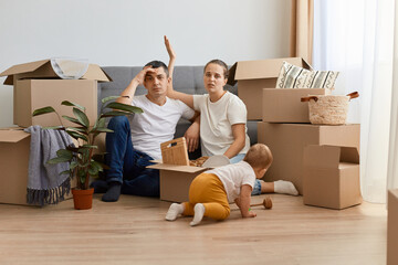 Unhappy young Caucasian couple having argument, sitting on floor in their new apartment on moving day. Stressed guy and his girlfriend quarelling during relocation.