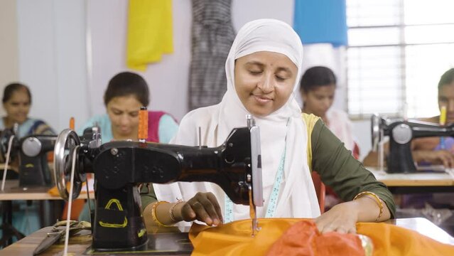 Happy smiling muslim woman in hijab loooking at camera while stitching using sawing machine at garments - concept of equality, diversity and employment