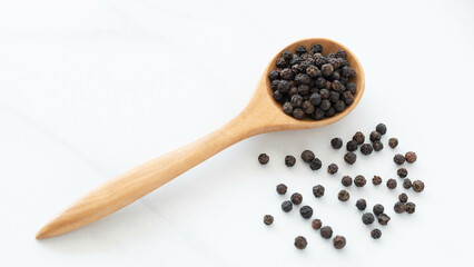 Black peppercorn with a wooden spoon on white background. Composition isolated over the white background.