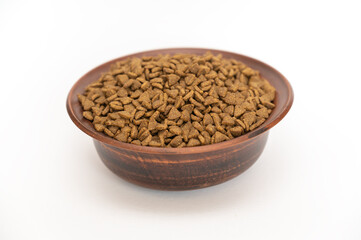 Pet food. Dry pelleted food in a brown clay bowl against a white background. The pellets are triangular.